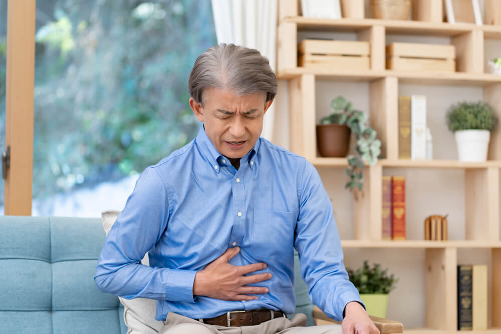 胃痛でお腹を抑える男性、胃酸が逆流し吐き気もある。